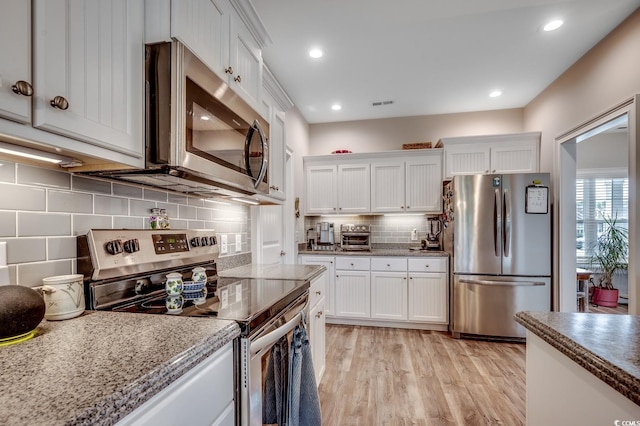 kitchen featuring decorative backsplash, appliances with stainless steel finishes, light wood-style floors, and white cabinetry