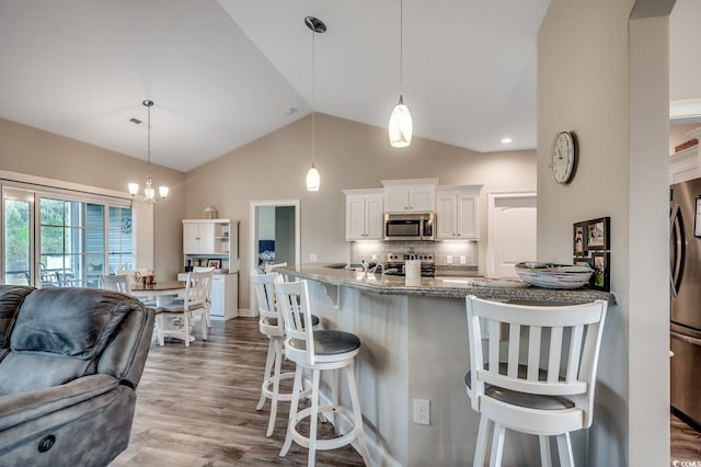 kitchen featuring backsplash, wood finished floors, appliances with stainless steel finishes, a breakfast bar area, and white cabinetry