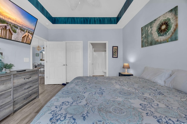 bedroom with wood finished floors, a towering ceiling, ensuite bathroom, and a ceiling fan