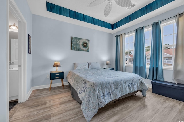 bedroom featuring light wood-type flooring, baseboards, ceiling fan, and ensuite bathroom
