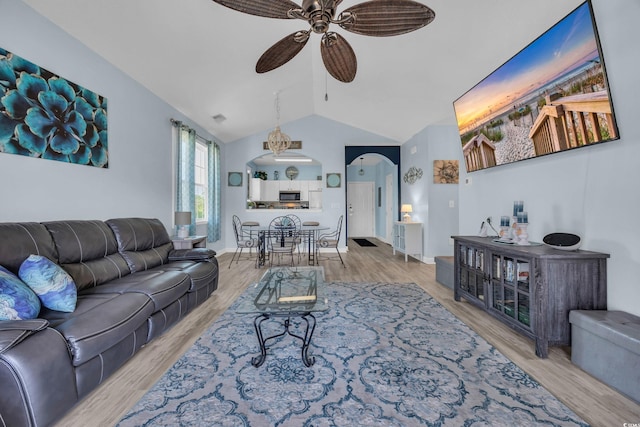 living room with a ceiling fan, arched walkways, vaulted ceiling, and wood finished floors