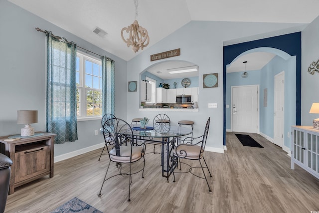 dining space featuring baseboards, lofted ceiling, wood finished floors, arched walkways, and a chandelier