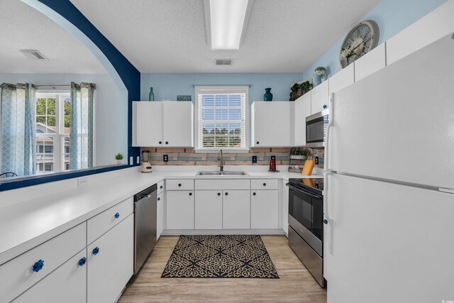 kitchen featuring appliances with stainless steel finishes, a sink, tasteful backsplash, light countertops, and white cabinetry
