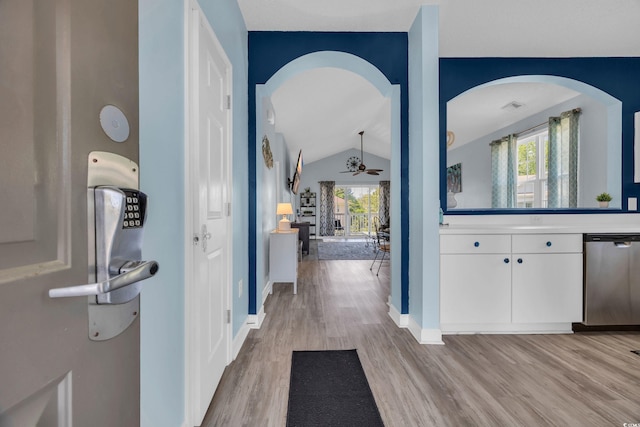 hallway with light wood-type flooring, healthy amount of natural light, vaulted ceiling, arched walkways, and baseboards