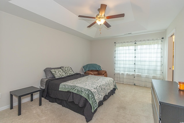bedroom featuring a ceiling fan, visible vents, light colored carpet, and a tray ceiling