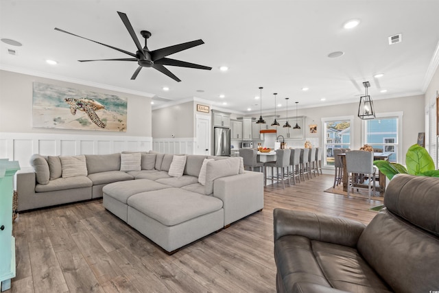 living room featuring a ceiling fan, light wood-type flooring, visible vents, ornamental molding, and recessed lighting