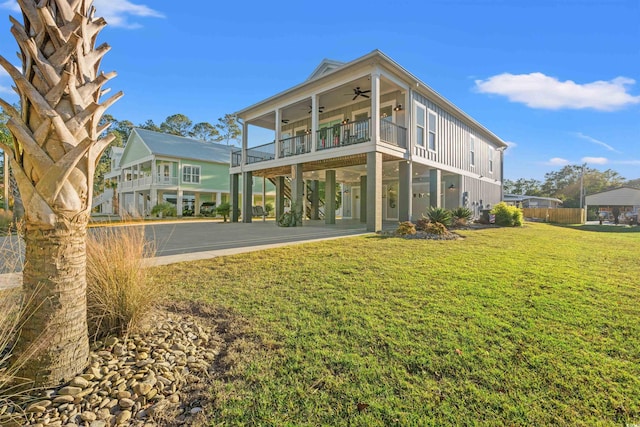 rear view of property featuring board and batten siding, driveway, a carport, a ceiling fan, and a lawn