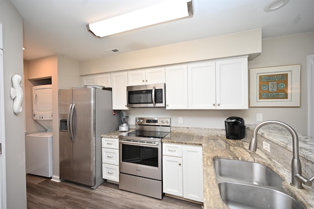 kitchen with white cabinets, stainless steel appliances, a sink, stacked washer / dryer, and wood finished floors