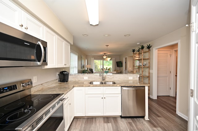 kitchen with a peninsula, light wood-style floors, stainless steel appliances, and a sink