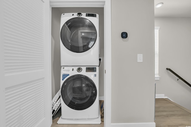 clothes washing area with stacked washer and clothes dryer, wood finished floors, and baseboards