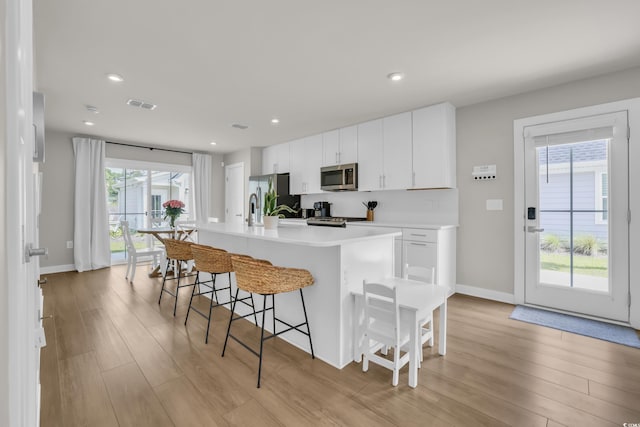 kitchen with appliances with stainless steel finishes, a kitchen bar, light wood-type flooring, an island with sink, and white cabinets