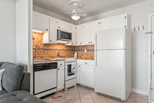 kitchen with decorative backsplash, a sink, white cabinets, white appliances, and light tile patterned flooring