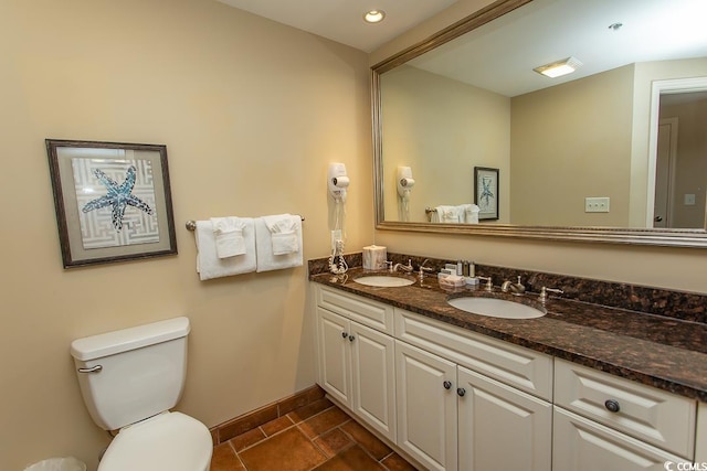 bathroom with double vanity, toilet, baseboards, and a sink
