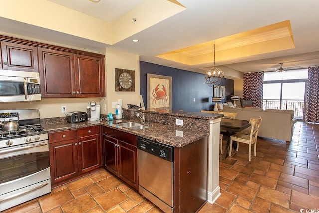 kitchen with a peninsula, open floor plan, a tray ceiling, a sink, and stainless steel appliances