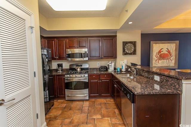 kitchen featuring a peninsula, dark stone counters, a sink, stone finish flooring, and stainless steel appliances