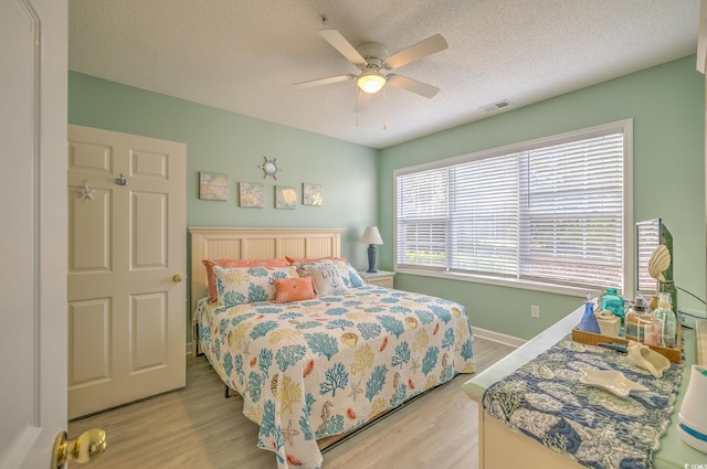 bedroom with light wood-type flooring, ceiling fan, baseboards, visible vents, and a textured ceiling