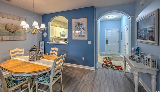 dining area featuring a chandelier, visible vents, baseboards, arched walkways, and wood finished floors