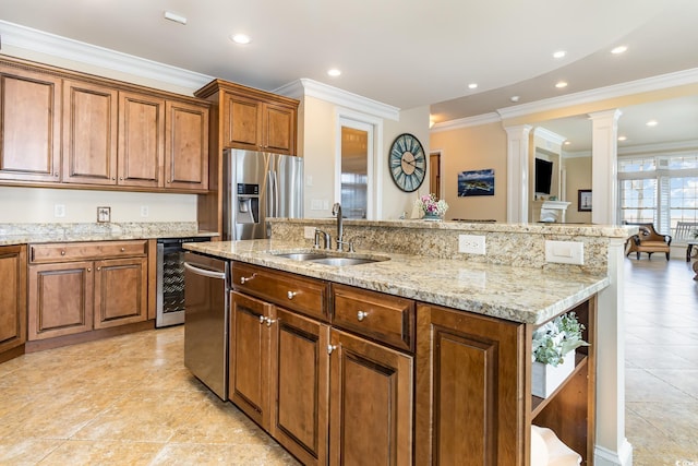 kitchen featuring a sink, beverage cooler, brown cabinetry, stainless steel appliances, and a center island with sink
