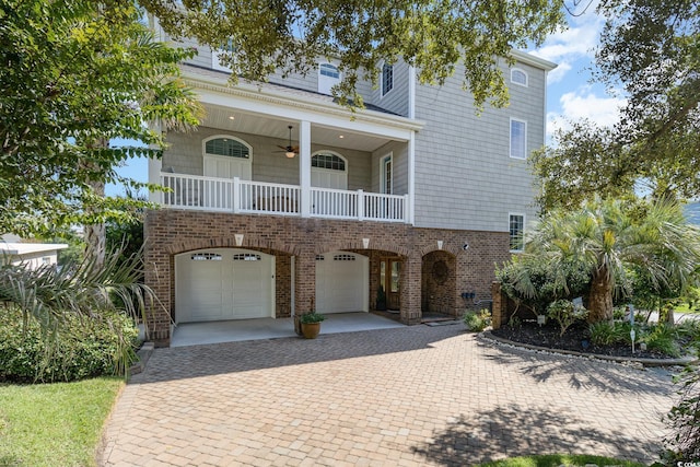 coastal inspired home with an attached garage, a ceiling fan, brick siding, and decorative driveway