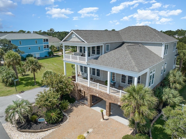 back of property with a balcony, decorative driveway, roof with shingles, a porch, and a carport