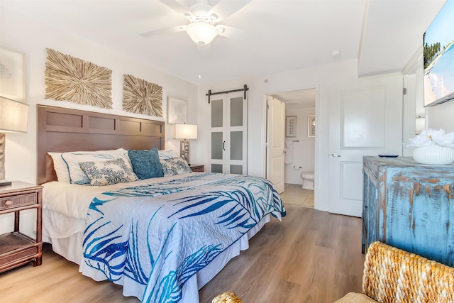 bedroom with ceiling fan, a barn door, wood finished floors, and ensuite bath