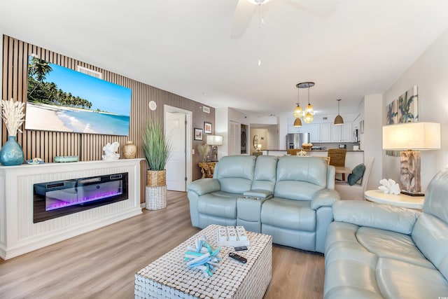 living room featuring light wood-style floors, a ceiling fan, and a glass covered fireplace