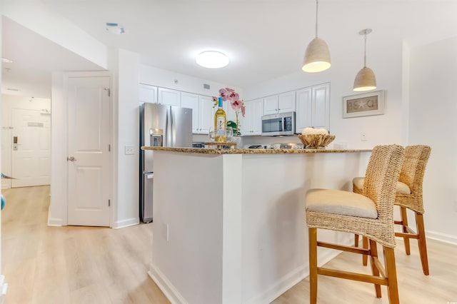 kitchen with appliances with stainless steel finishes, hanging light fixtures, light wood-type flooring, baseboards, and dark stone countertops