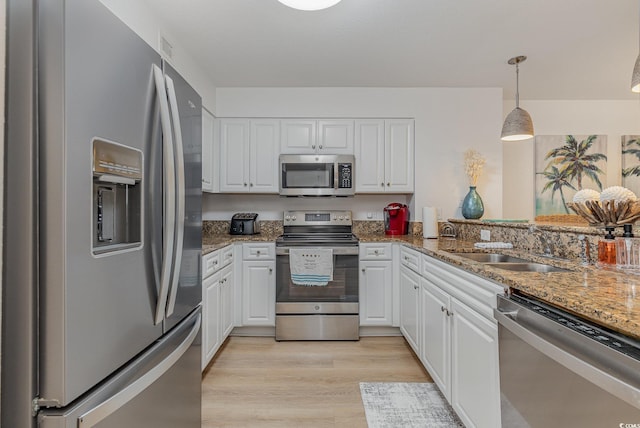 kitchen with white cabinets, appliances with stainless steel finishes, a sink, light wood finished floors, and stone counters