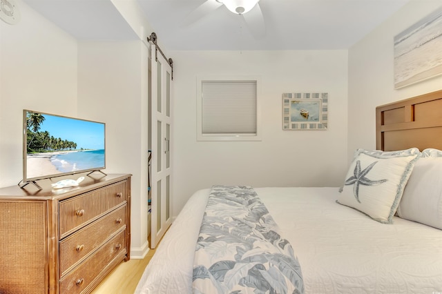 bedroom with light wood-style floors, a ceiling fan, and a barn door
