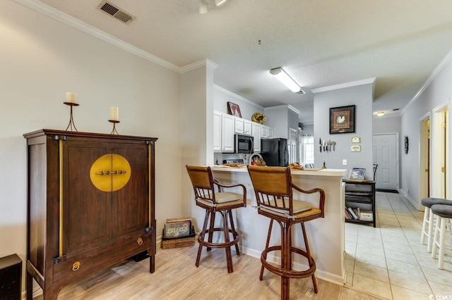 kitchen featuring freestanding refrigerator, a breakfast bar, a peninsula, ornamental molding, and white cabinets