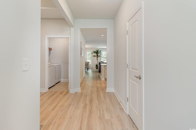 hallway with light wood-type flooring, baseboards, and washer and clothes dryer