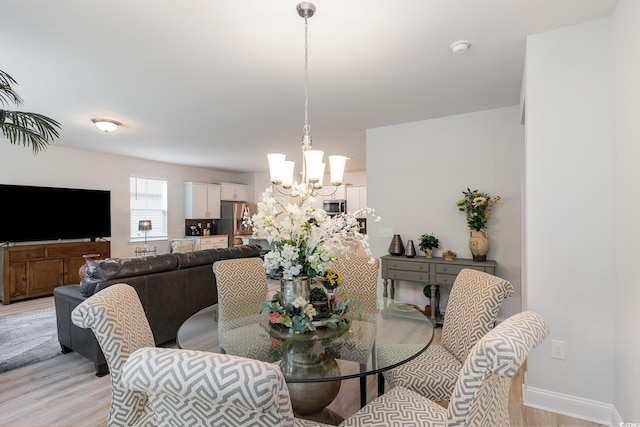 dining area with a chandelier, light wood-style floors, and baseboards