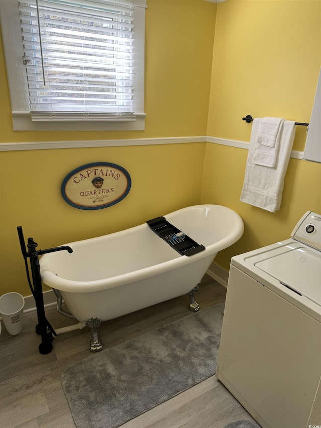 bathroom featuring baseboards, wood finished floors, a soaking tub, and washer / clothes dryer