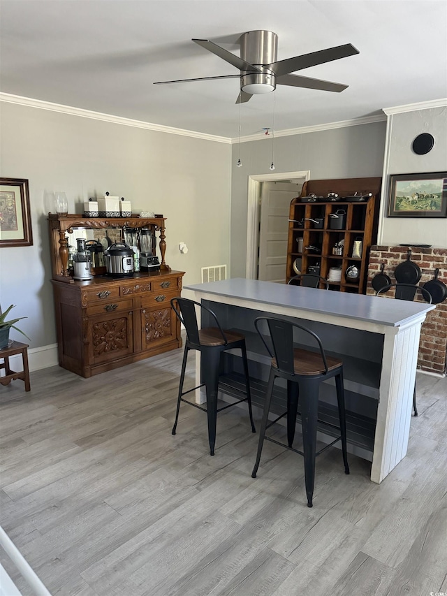 dining space with light wood-style floors, ornamental molding, a ceiling fan, and visible vents