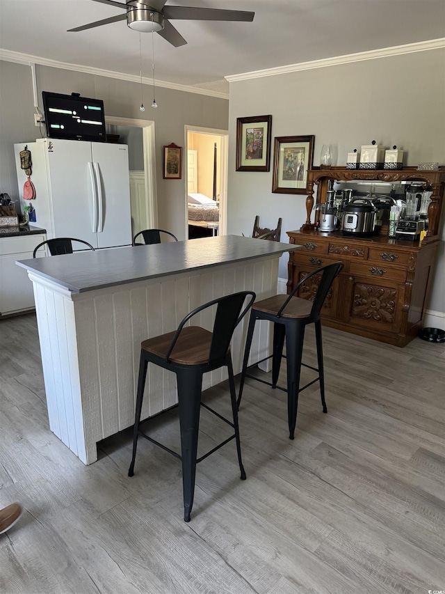 kitchen with ceiling fan, a kitchen bar, light wood finished floors, and freestanding refrigerator