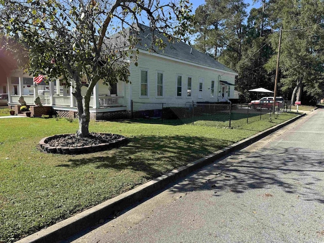 view of side of home featuring fence, covered porch, and a yard
