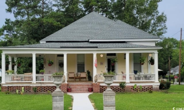 farmhouse featuring a porch, a front yard, and roof with shingles
