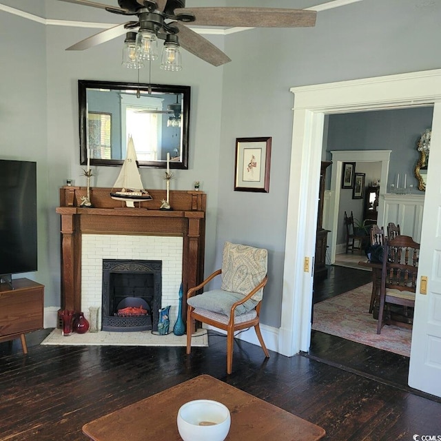 living area featuring baseboards, a ceiling fan, a brick fireplace, and hardwood / wood-style flooring