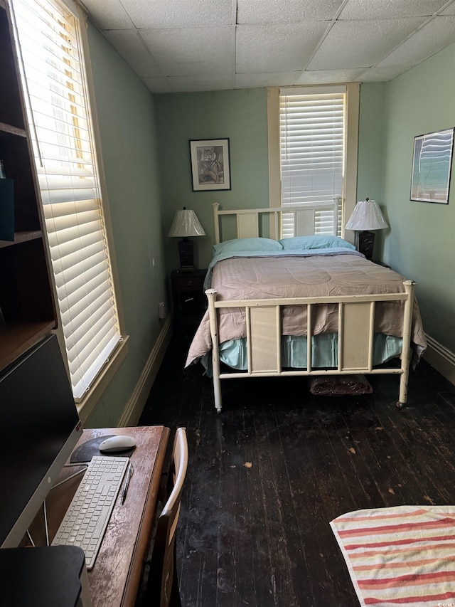 bedroom with a paneled ceiling, hardwood / wood-style flooring, and baseboards