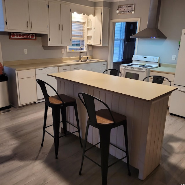 kitchen with white appliances, light wood-type flooring, wall chimney exhaust hood, white cabinetry, and a sink