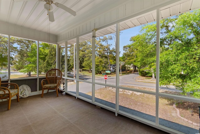 sunroom featuring a ceiling fan and view of wooded area