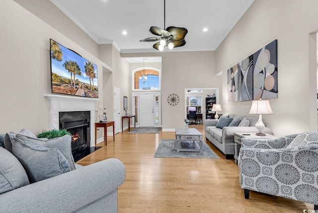living room with ceiling fan, crown molding, a high end fireplace, light wood-style floors, and a high ceiling