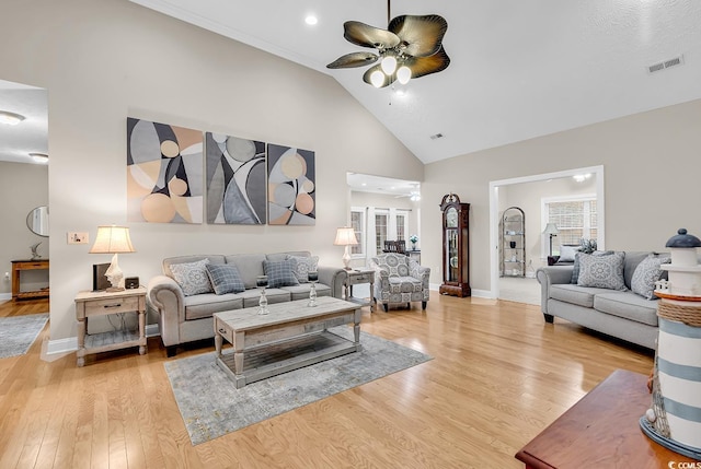 living room featuring visible vents, light wood-style floors, baseboards, ceiling fan, and high vaulted ceiling
