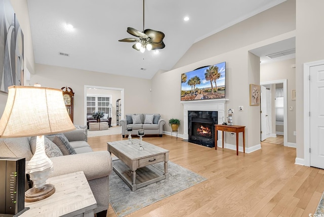 living room featuring light wood finished floors, a ceiling fan, lofted ceiling, a high end fireplace, and visible vents