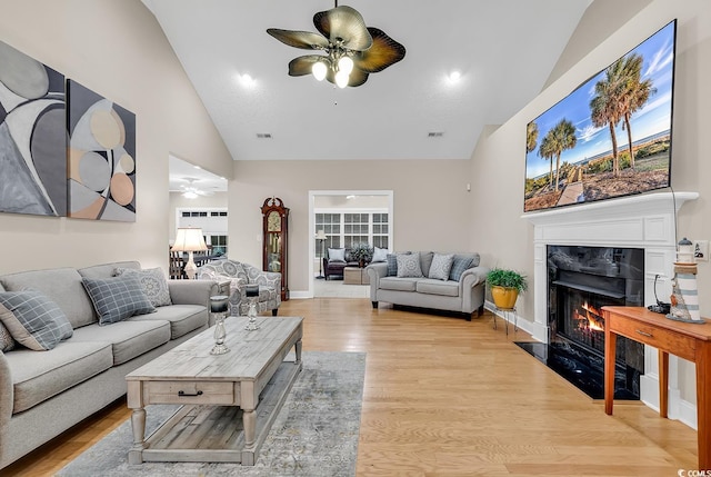 living room with high vaulted ceiling, a fireplace, a ceiling fan, and light wood-style flooring
