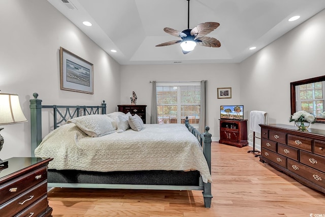 bedroom with multiple windows, a ceiling fan, a tray ceiling, and light wood-style flooring