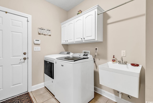 washroom with baseboards, separate washer and dryer, a sink, cabinet space, and light tile patterned floors