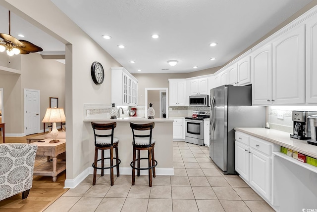 kitchen featuring glass insert cabinets, ceiling fan, a kitchen breakfast bar, tasteful backsplash, and appliances with stainless steel finishes