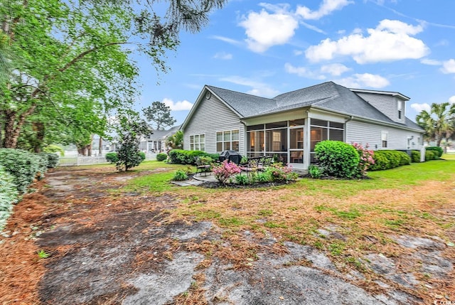 rear view of property with a lawn, a patio, a shingled roof, and a sunroom