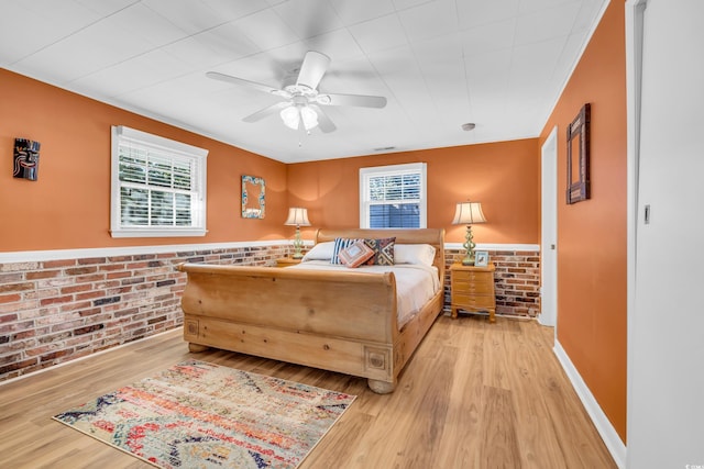 bedroom with wainscoting, ceiling fan, wood finished floors, and brick wall